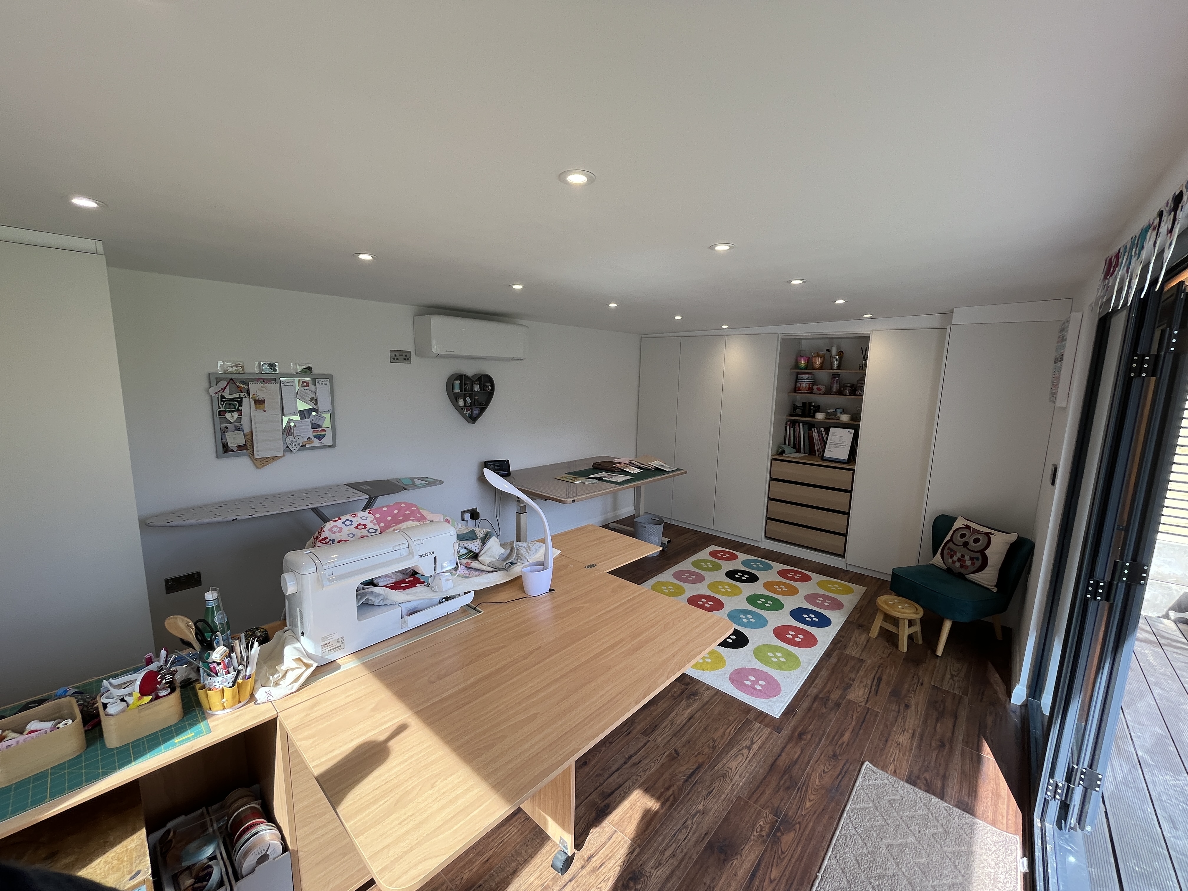 Modern home office with large glass doors, featuring cosy armchairs, a stylish desk with ergonomic chairs, and a serene view of lush greenery outside.