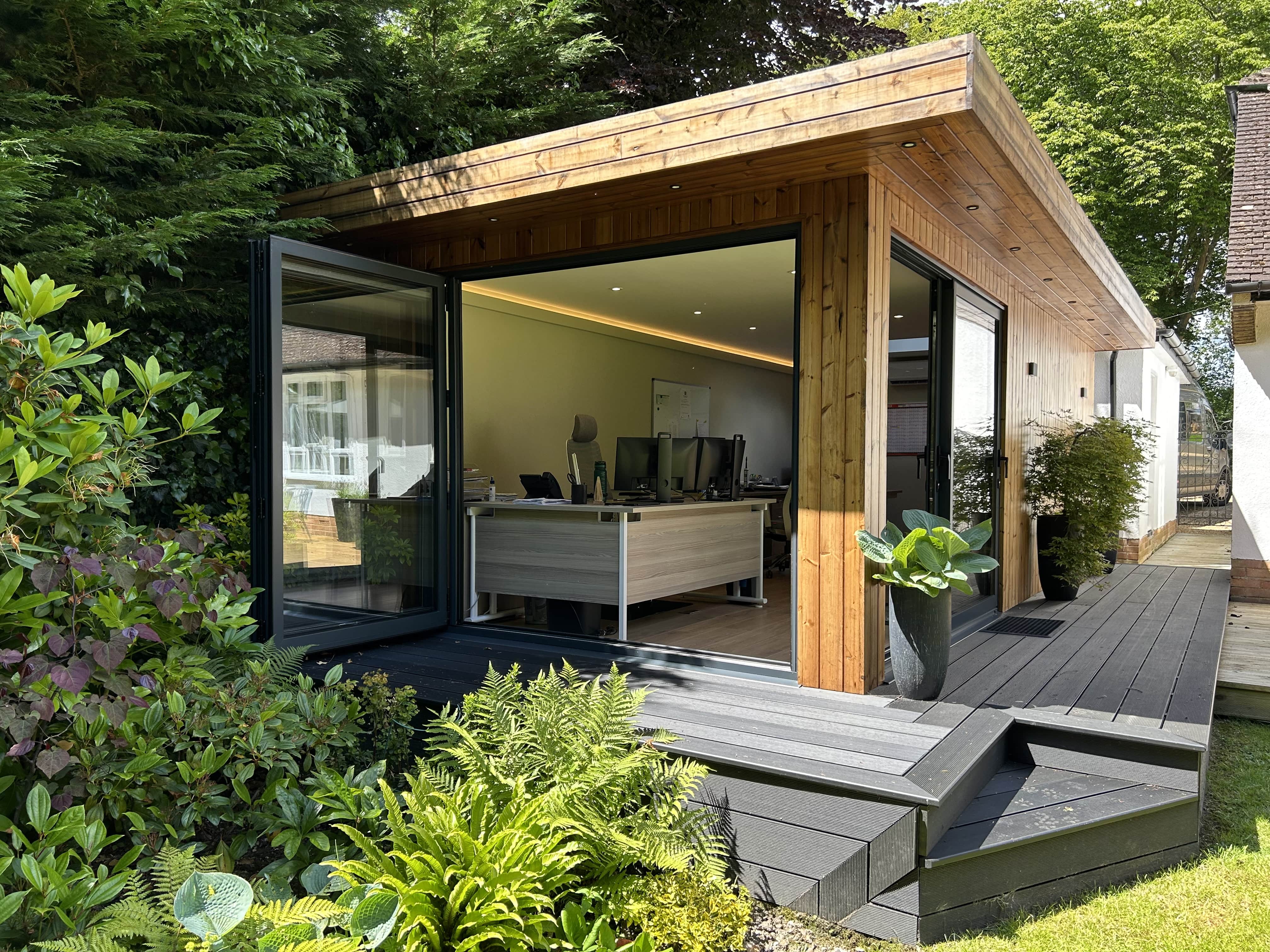 Contemporary garden office pod with large glass doors, wooden cladding, and lush green surroundings, providing a serene and stylish workspace.
