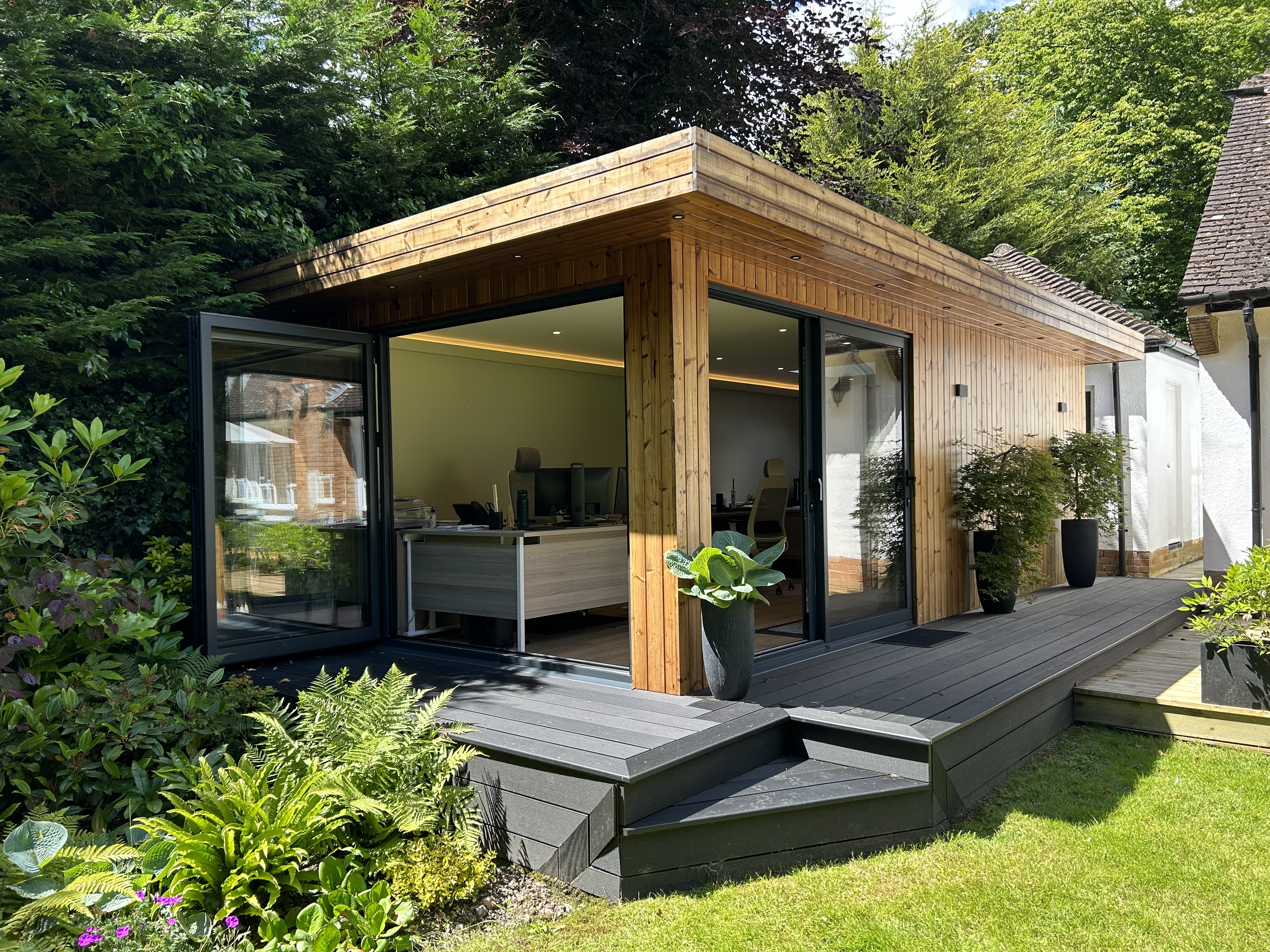 Contemporary garden office pod with large glass doors, wooden cladding, and lush green surroundings, providing a serene and stylish workspace.
