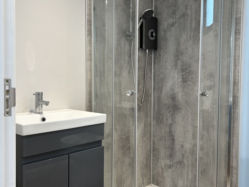 Modern bathroom with a grey textured shower enclosure, a glass door, and a sleek black vanity unit with a white sink and chrome fixtures.