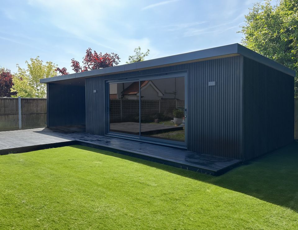Modern garden room with large glass doors, featuring a cosy seating area and a hot tub under a wooden pergola, surrounded by lush greenery and a well-manicured lawn.