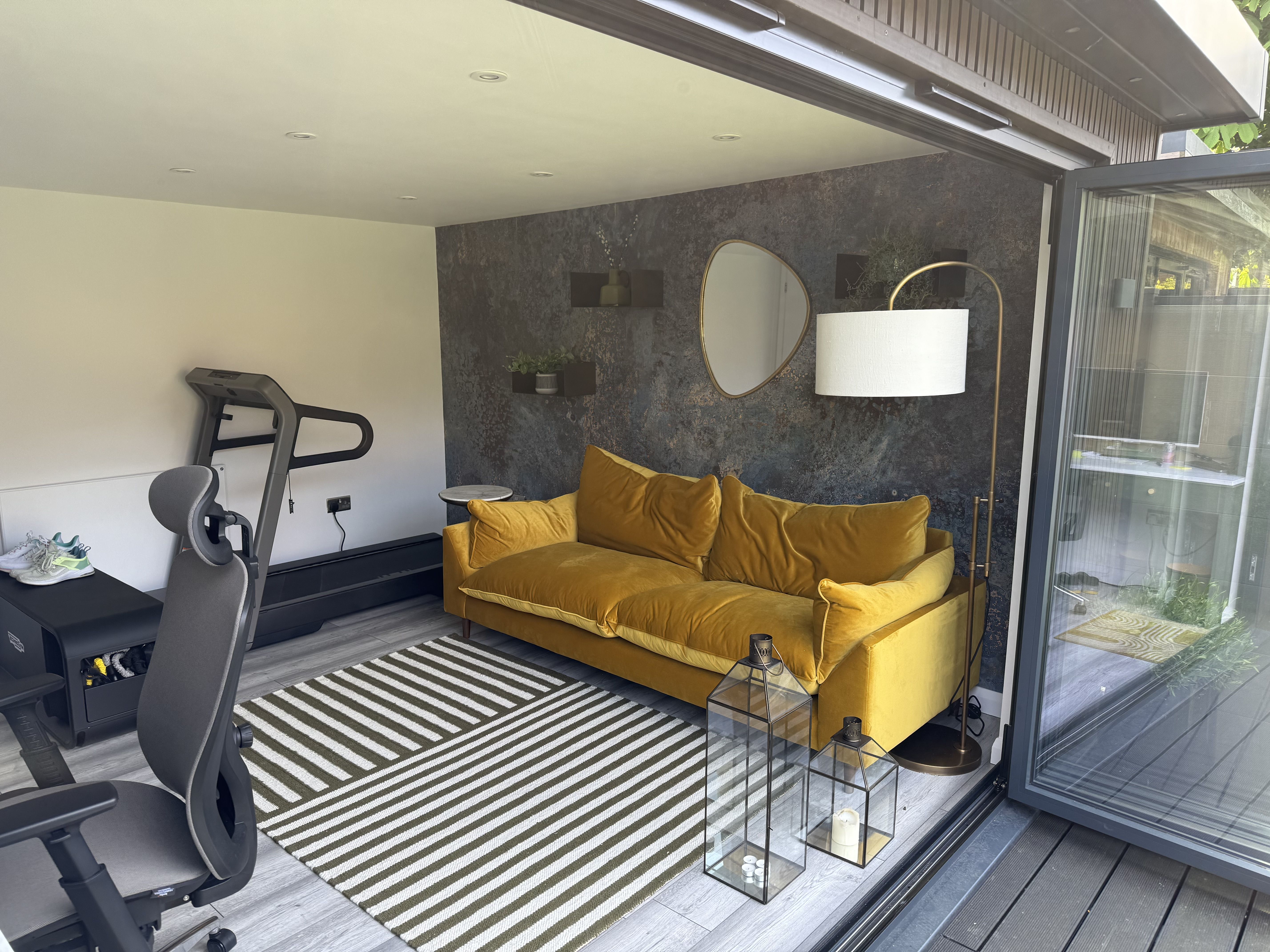 Cosy wooden garden office with large glass sliding doors, warm interior lighting, and a charming gravel pathway, nestled in a lush garden setting.
