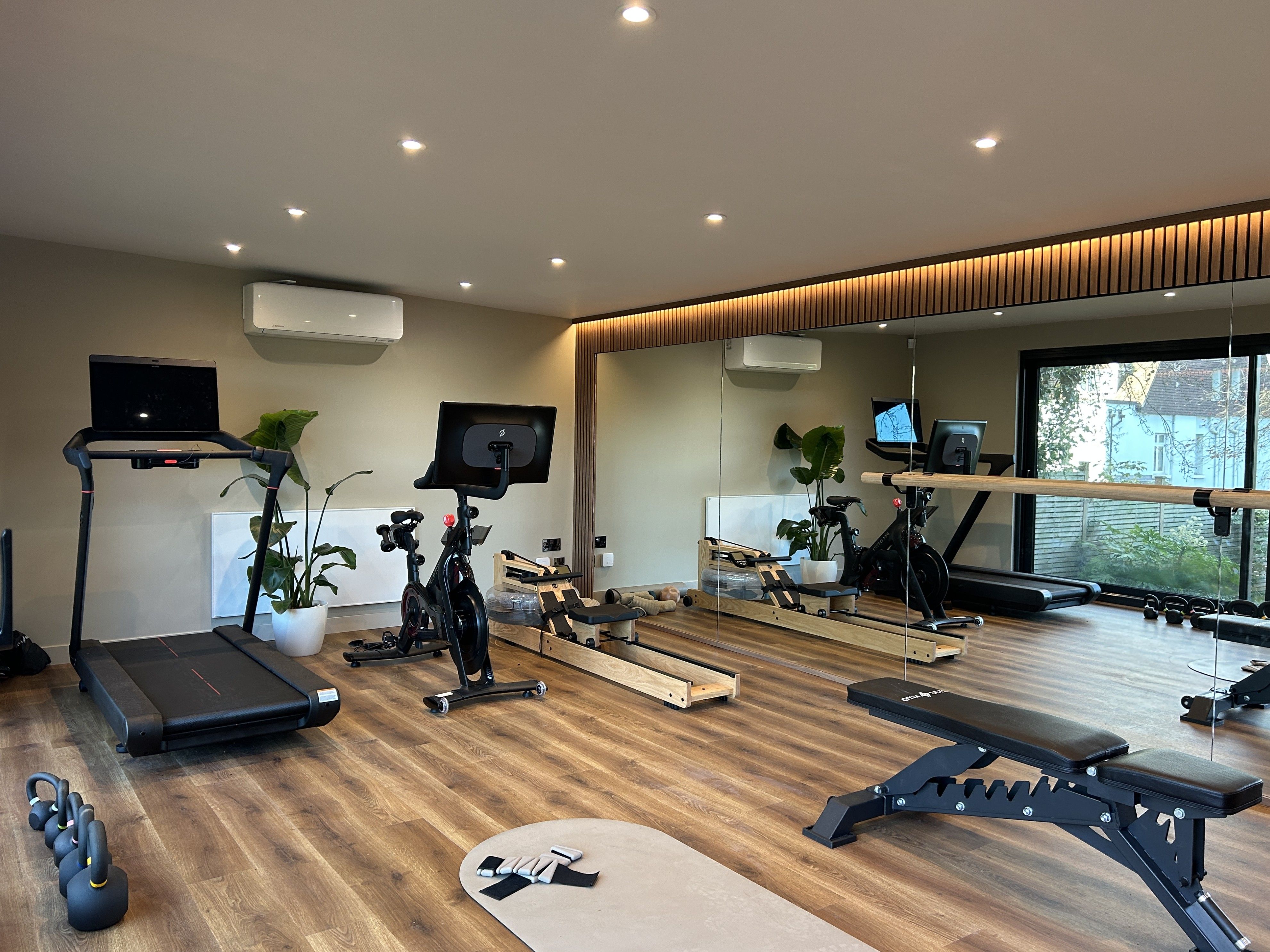 Charming garden room with large glass doors, featuring a cosy wooden deck and a white bench, nestled in a lush, tree-filled garden with a gravel pathway.